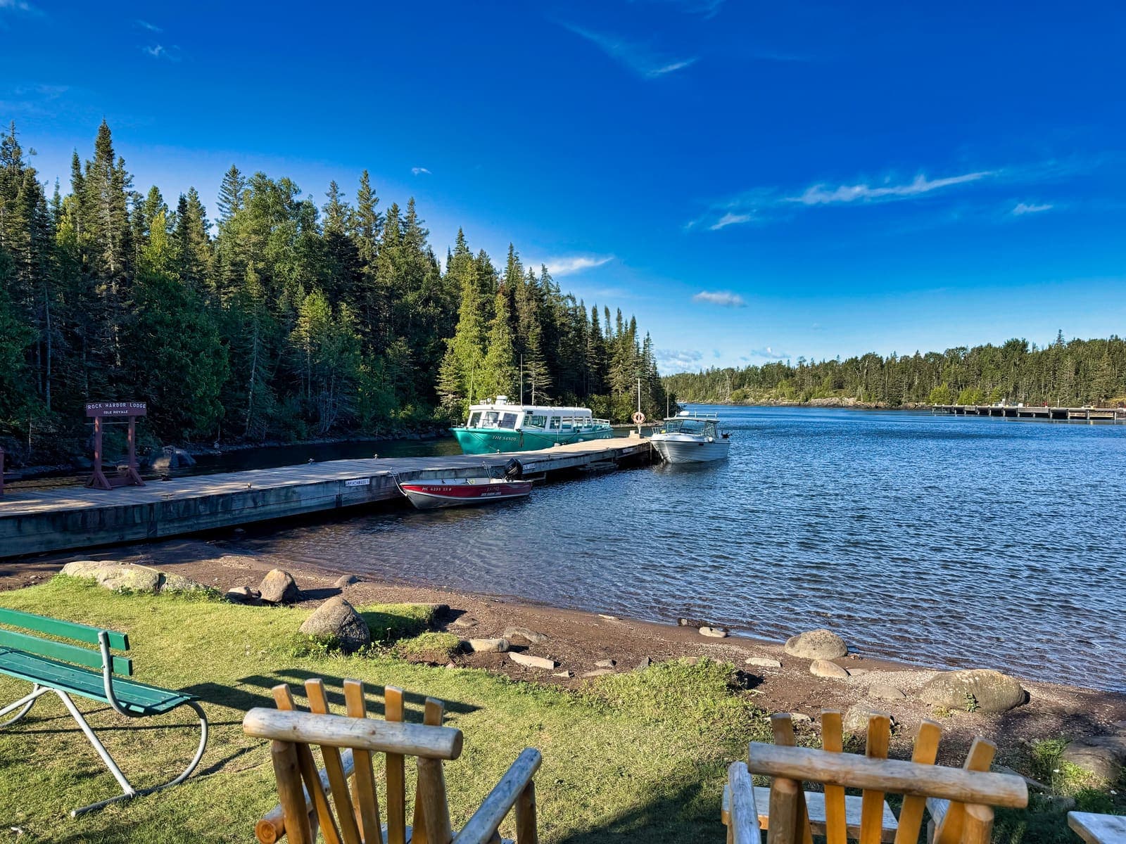 The Rock Harbor dock with a tour boat, a small red boat and empty chairs on the grass