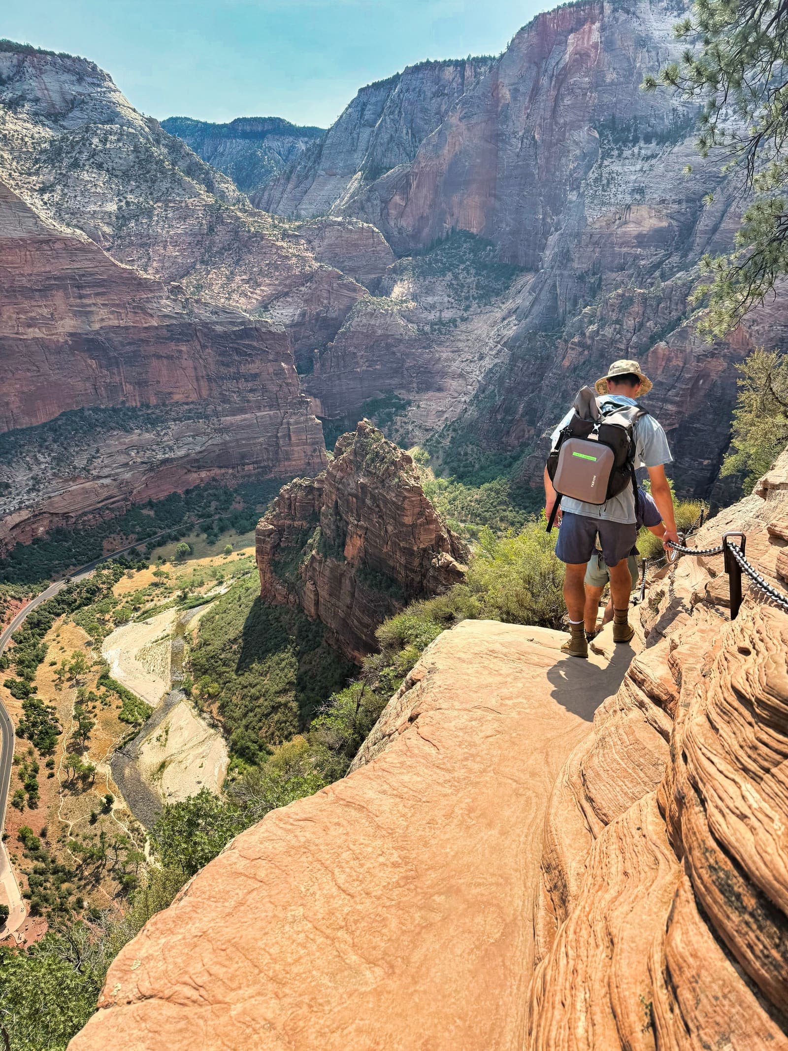 A hiker holding the chain on the knife-edge ridge of Angels Landing, the canyon floor far below